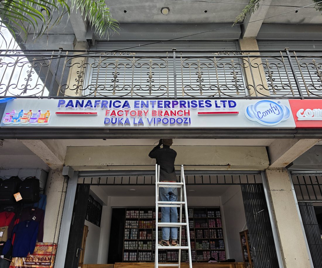 The HuRu Studios team installing custom signage on a storefront in Arusha, Tanzania